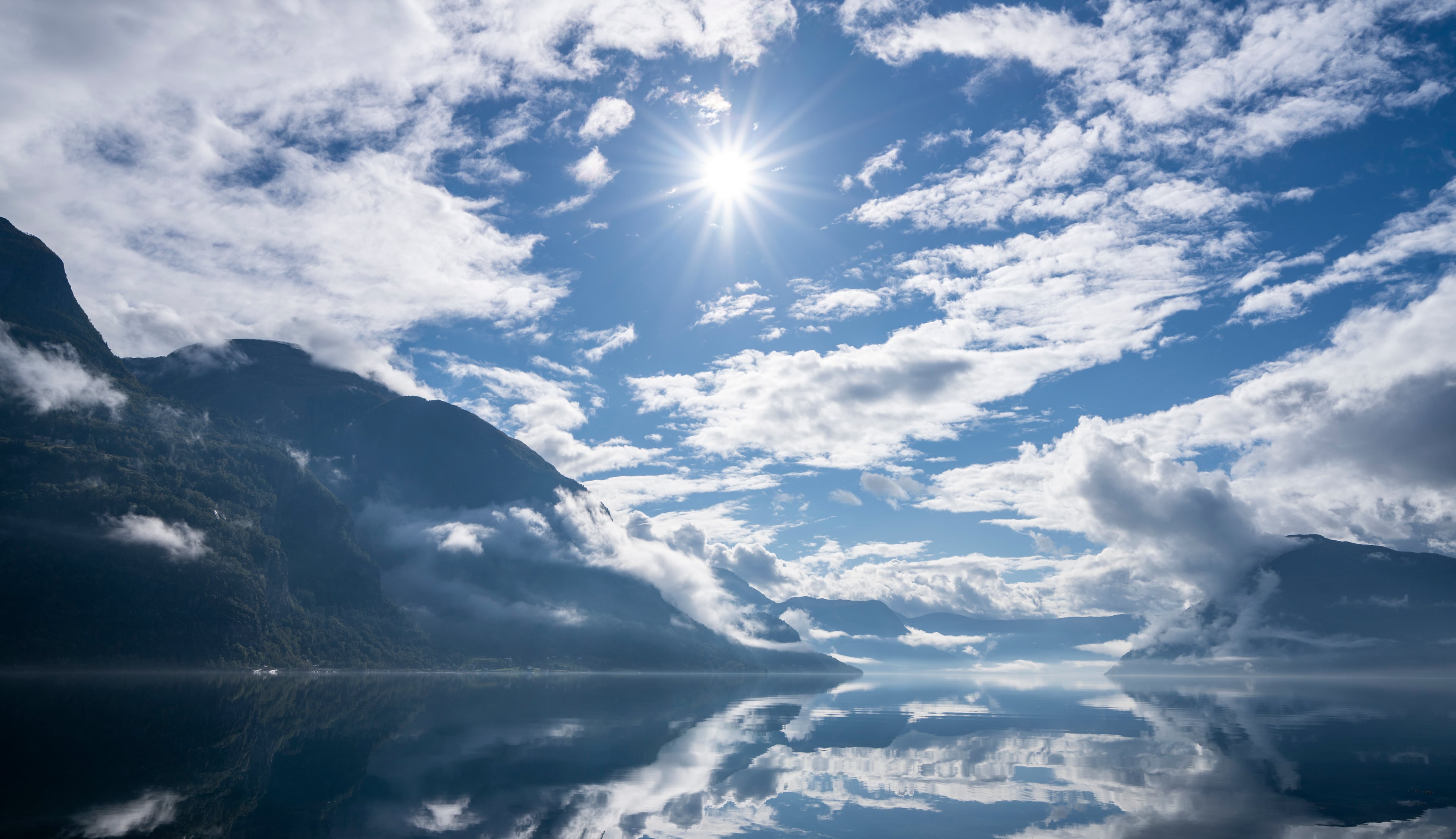 blank fjord omkransa av fjell med flekkvis snø 
