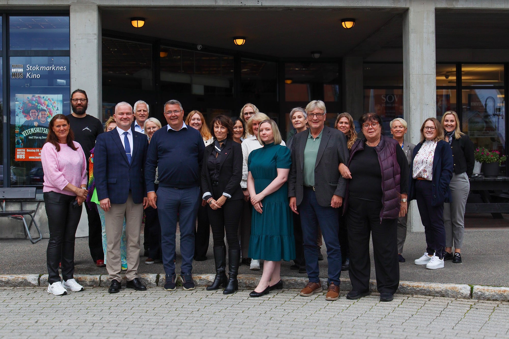 En gruppe mennesker står på et fortau foran inngangen til en stor bygning.