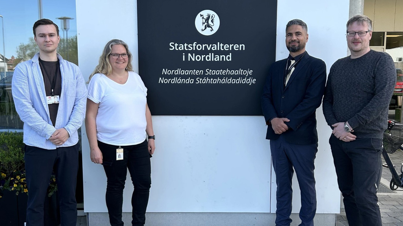 Fire personer står oppstilt foran kontorbygning.