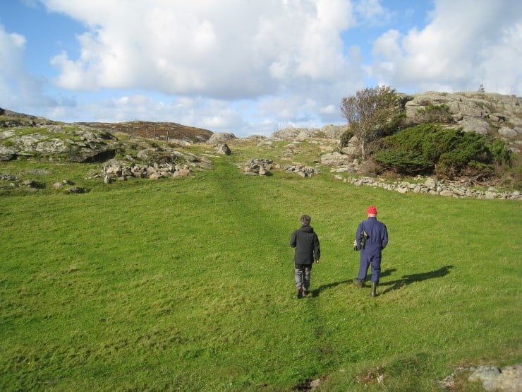 Skyer, blå himmel, grønt gras, to personer, berg og stein.