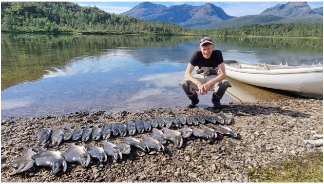 Mann sitter på huk ved elv. Ved siden av ligger det fisk som er fisket.