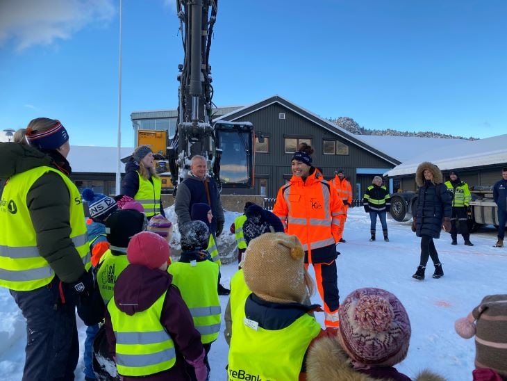 Barn og voksne som står fremfor en gravemaskin