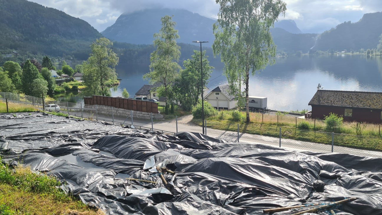 Svart plastduk på et jorde. Landskap og vann i bakgrunnen