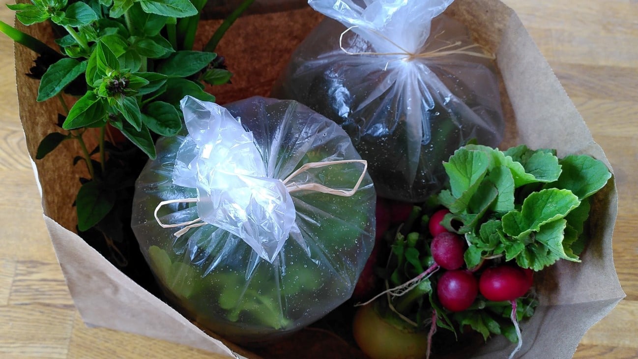 En papirpose med ulike grønsaker, nokre av dei pakka inn i plastposar