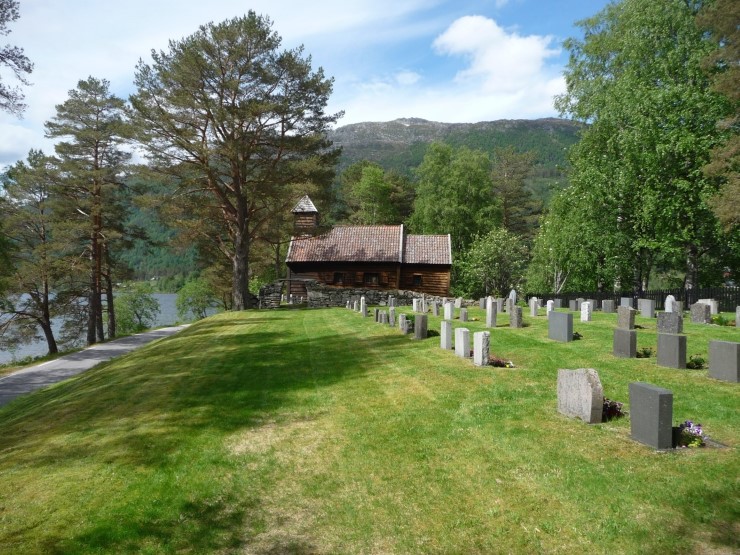 ei kyrkje i framgrunnen med rader med gravsteiner og grøn plen