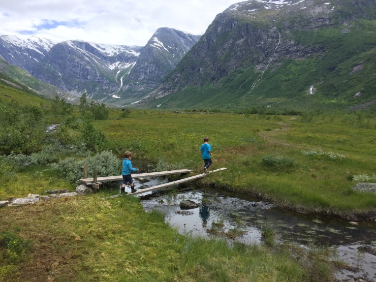 to gutar går over ei kloppebru med grønt landskap og fjell