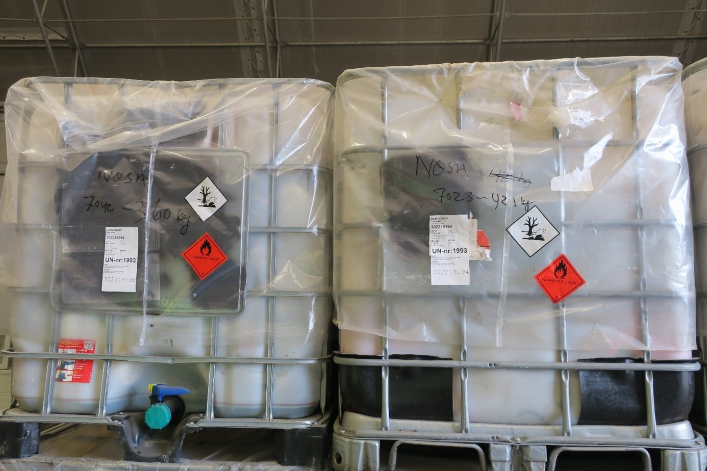 Bilde av tankar i plast som ligg inne i eit metallskrog. Dei er mekra med ulike klistremerke. Det er også skrive på kva som er oppi og kor mykje.  Dei er lagra innandørs. 