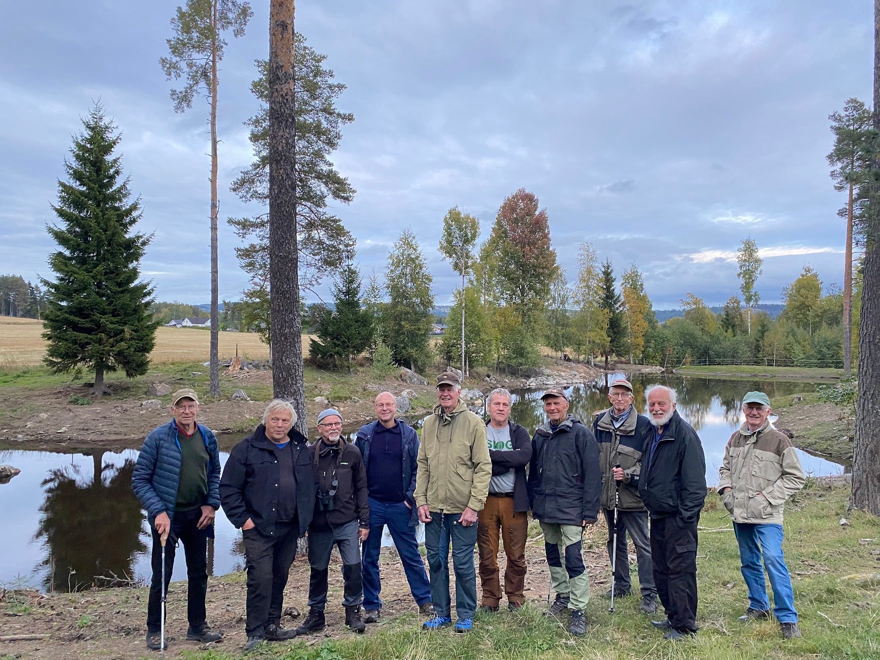 Gruppe med eldre menn står fremfor en dam.