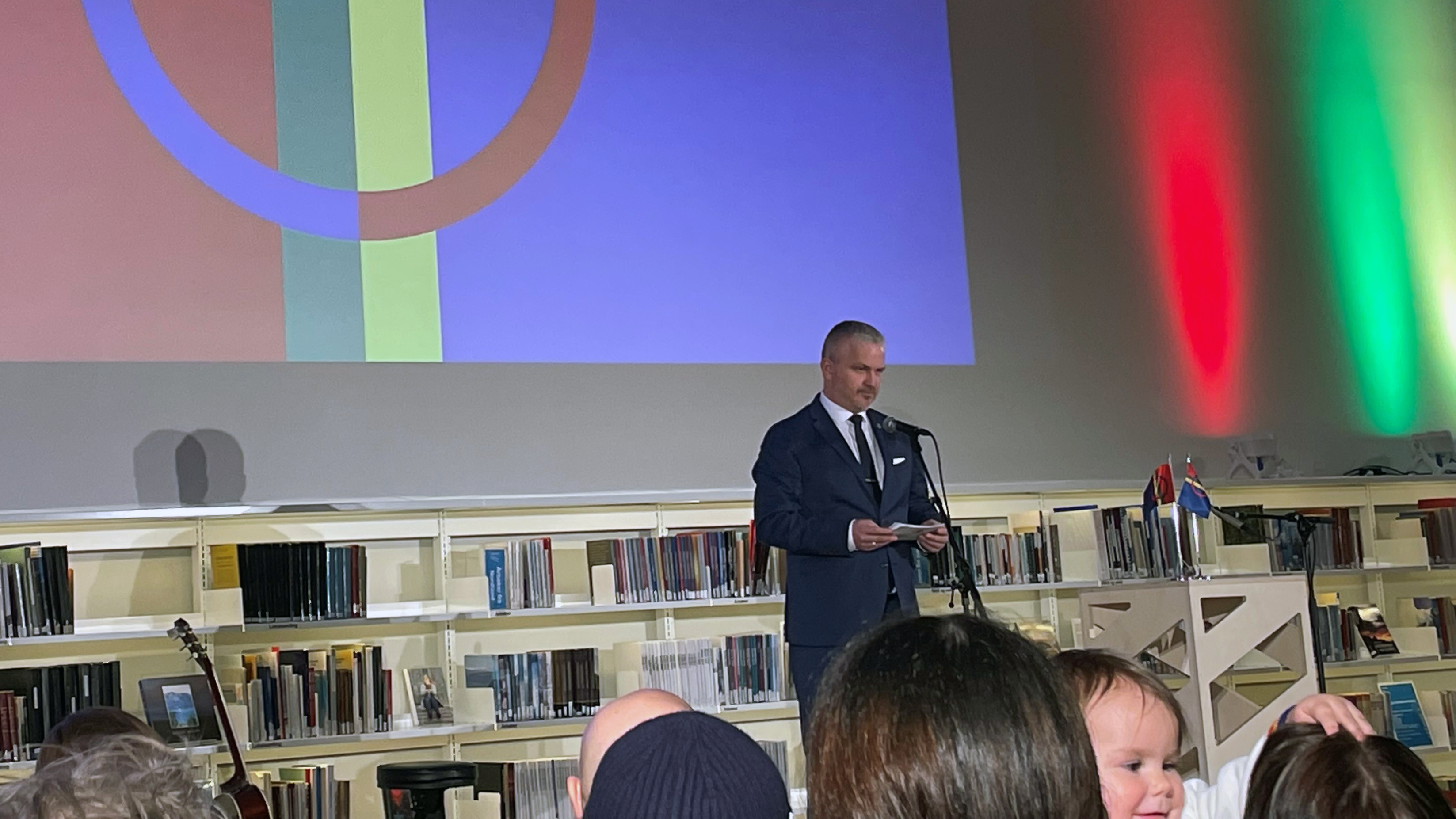 Mann i dress holder tale på scene i bibliotek.
