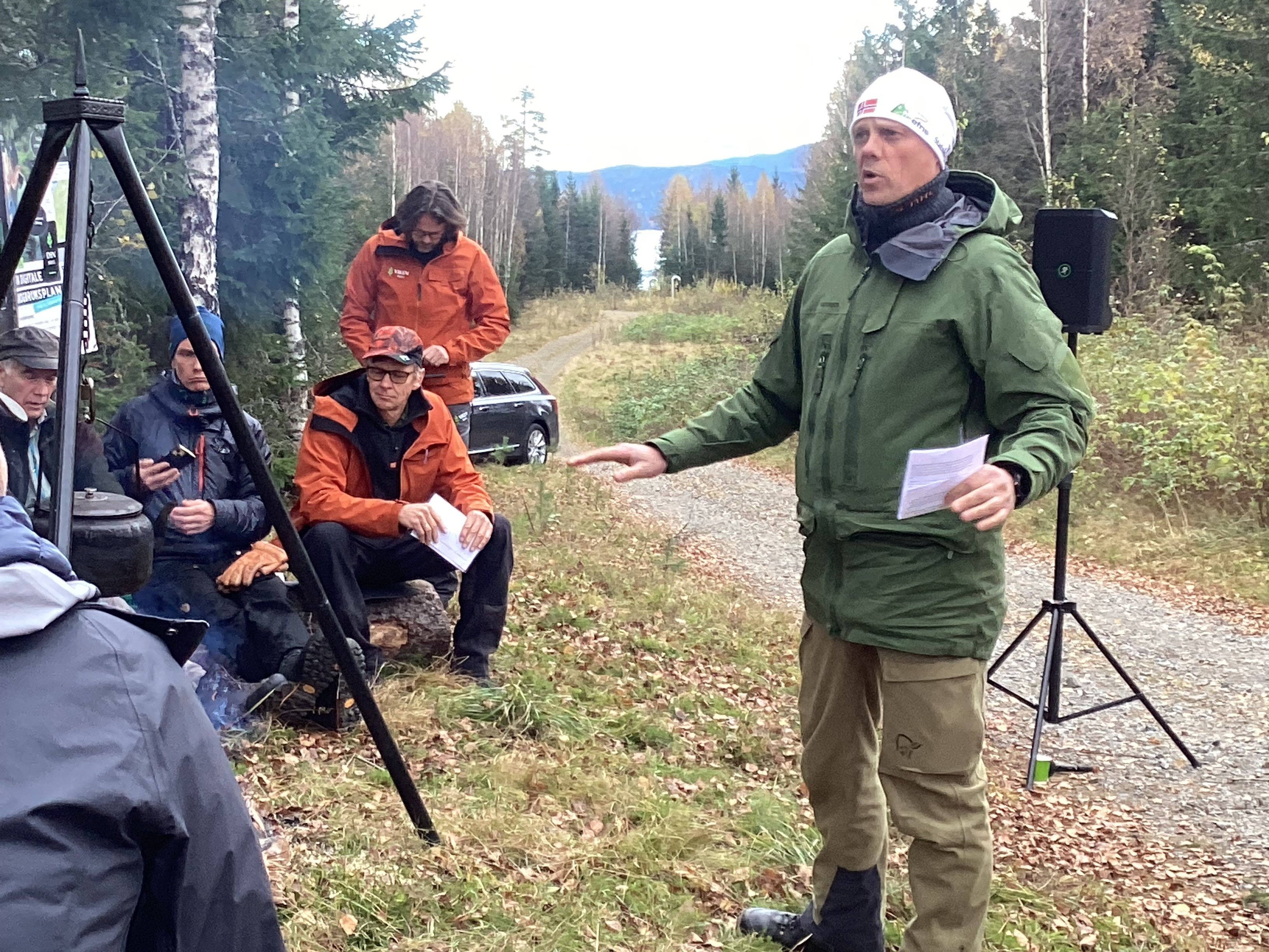 Bilde som viser skog, skogsbilvei, mennesker rundt et bål