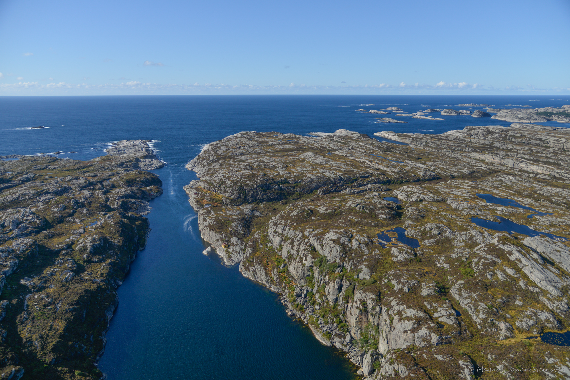 Eit landskap sett frå lufta med sjø og berg ut mot havet.