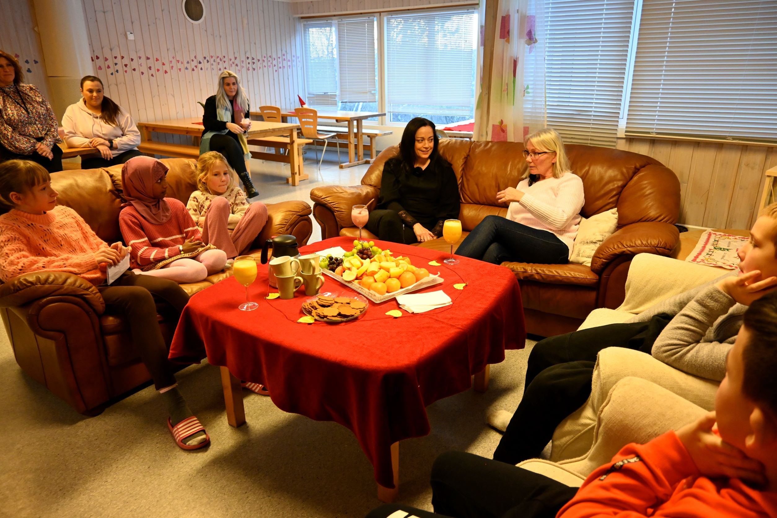 Bilde av barn frå SFO som sit rundt fruktfatet i lag med statsforvaltar Else-May Norderhus og Berit Ulriksborg som leiar SFO. 
