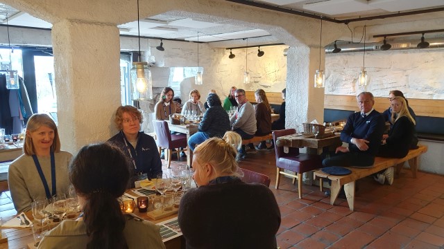 Bildet viser mennesker rundt bord, servering av lokalmat, steinkjeller