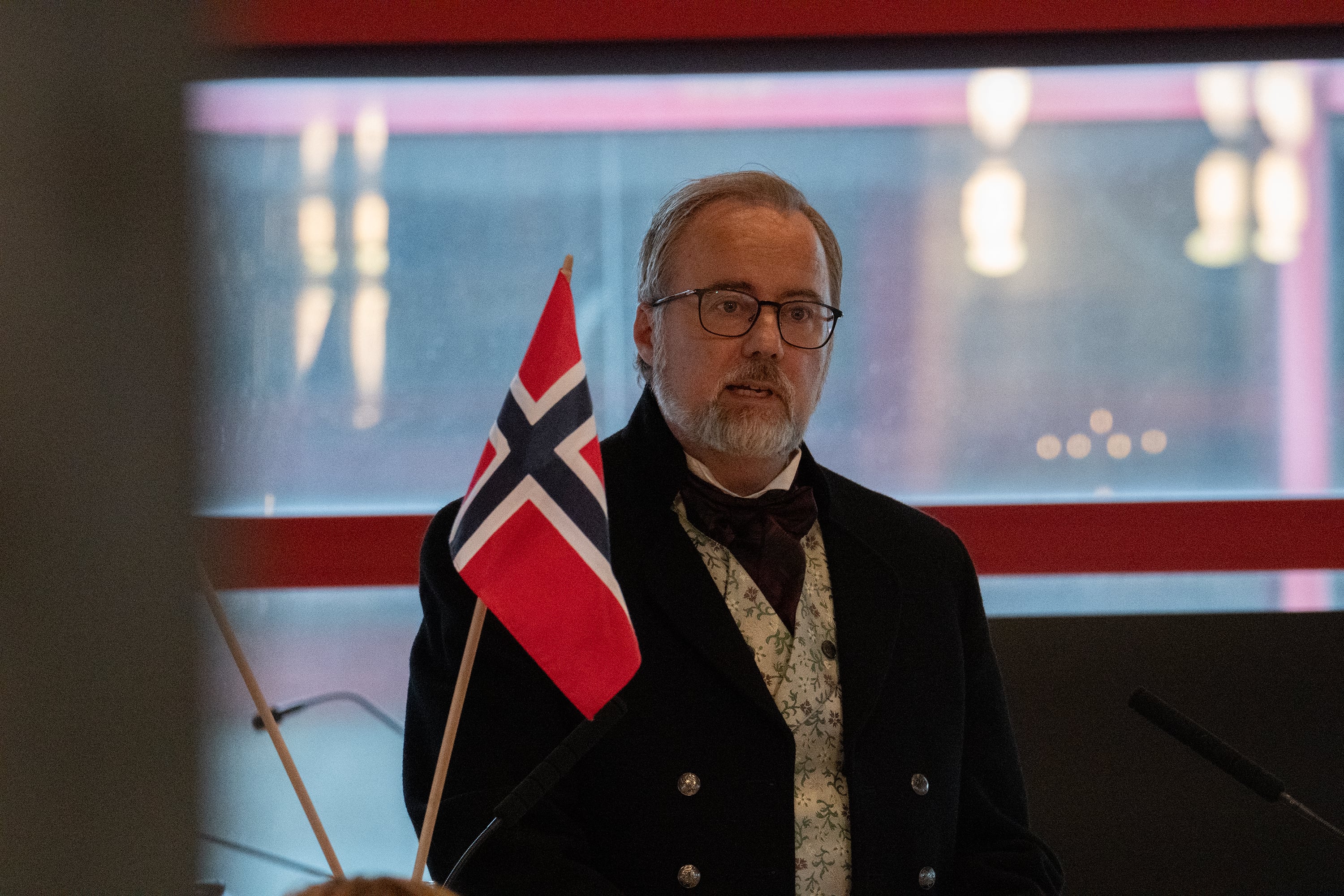 Mann i bunad står bak talerstol.