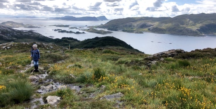 et barn går på sti på ei ås og det er kyst og hav i horisonten