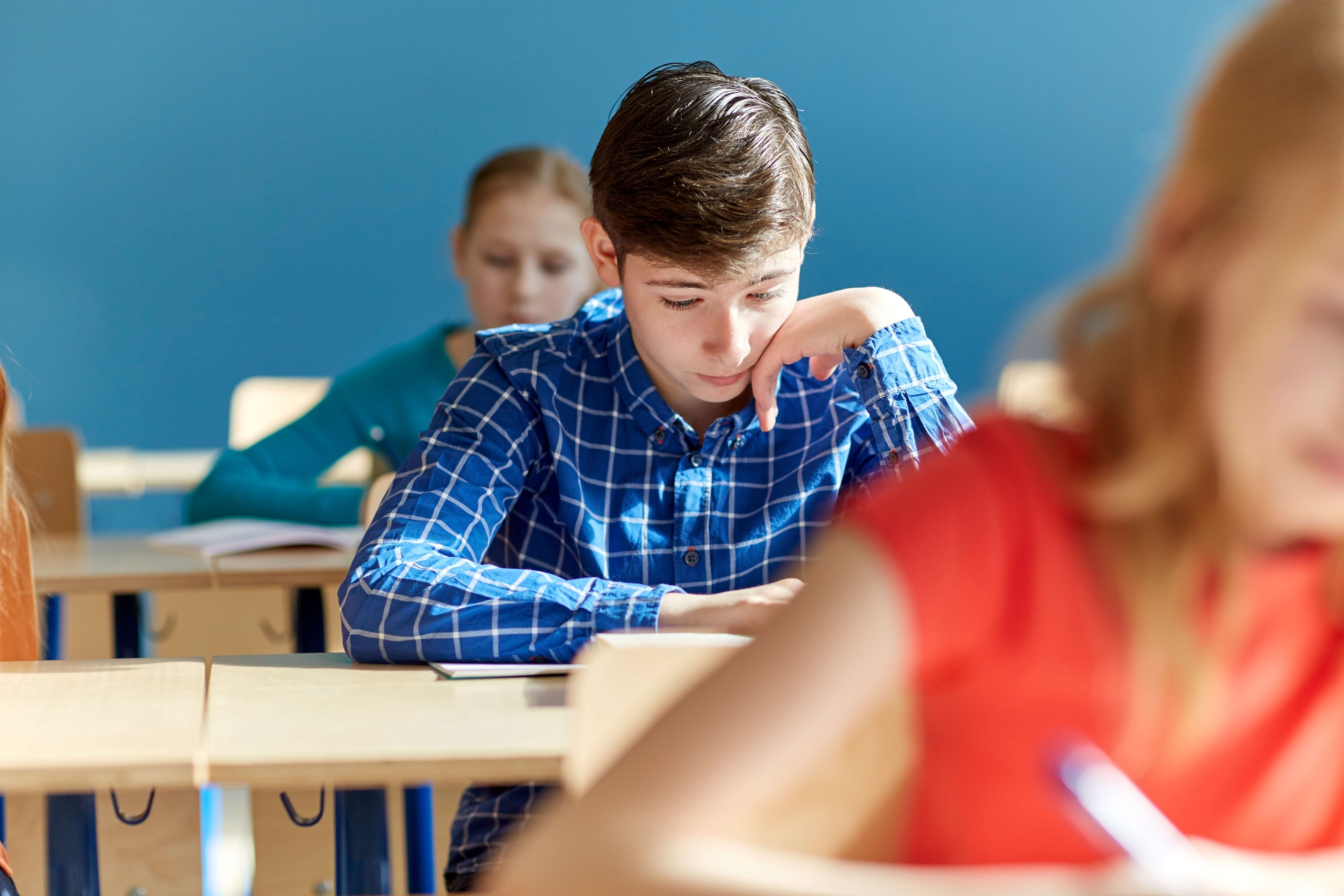 Gutt som sitter ved en pult på skolen og leser