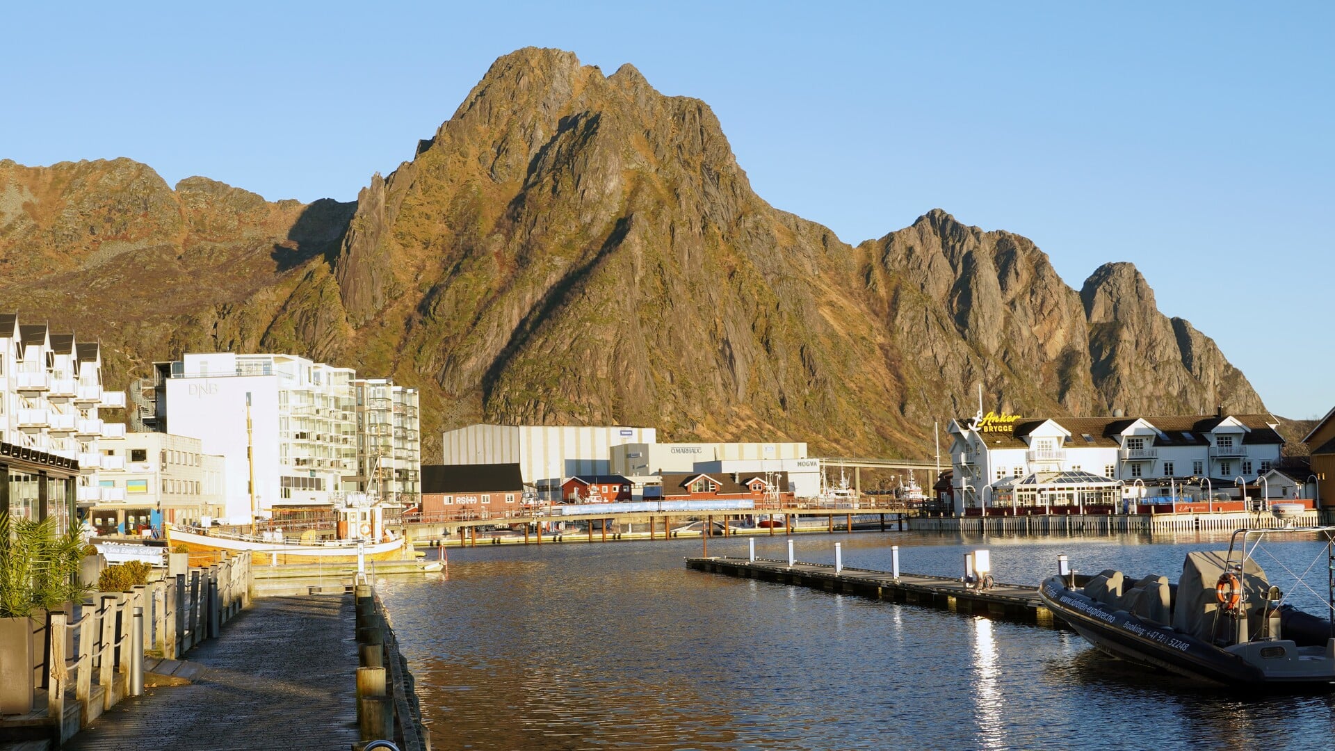 Havnepromenade, havn og bygninger med spisse fjell i bakgrunnen.