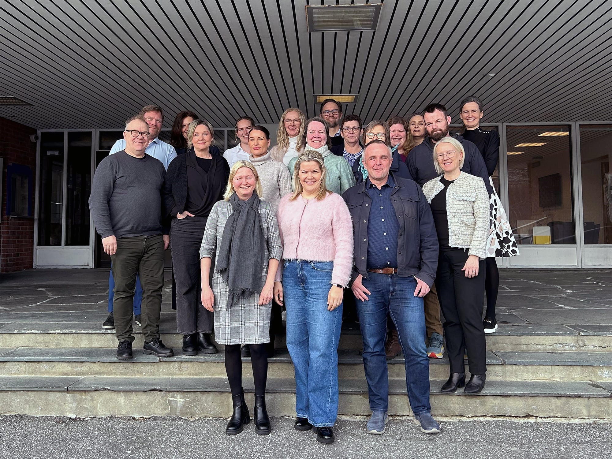 En gruppe mennesker står oppstilt i trapp foran inngangen til et kontorbygg.