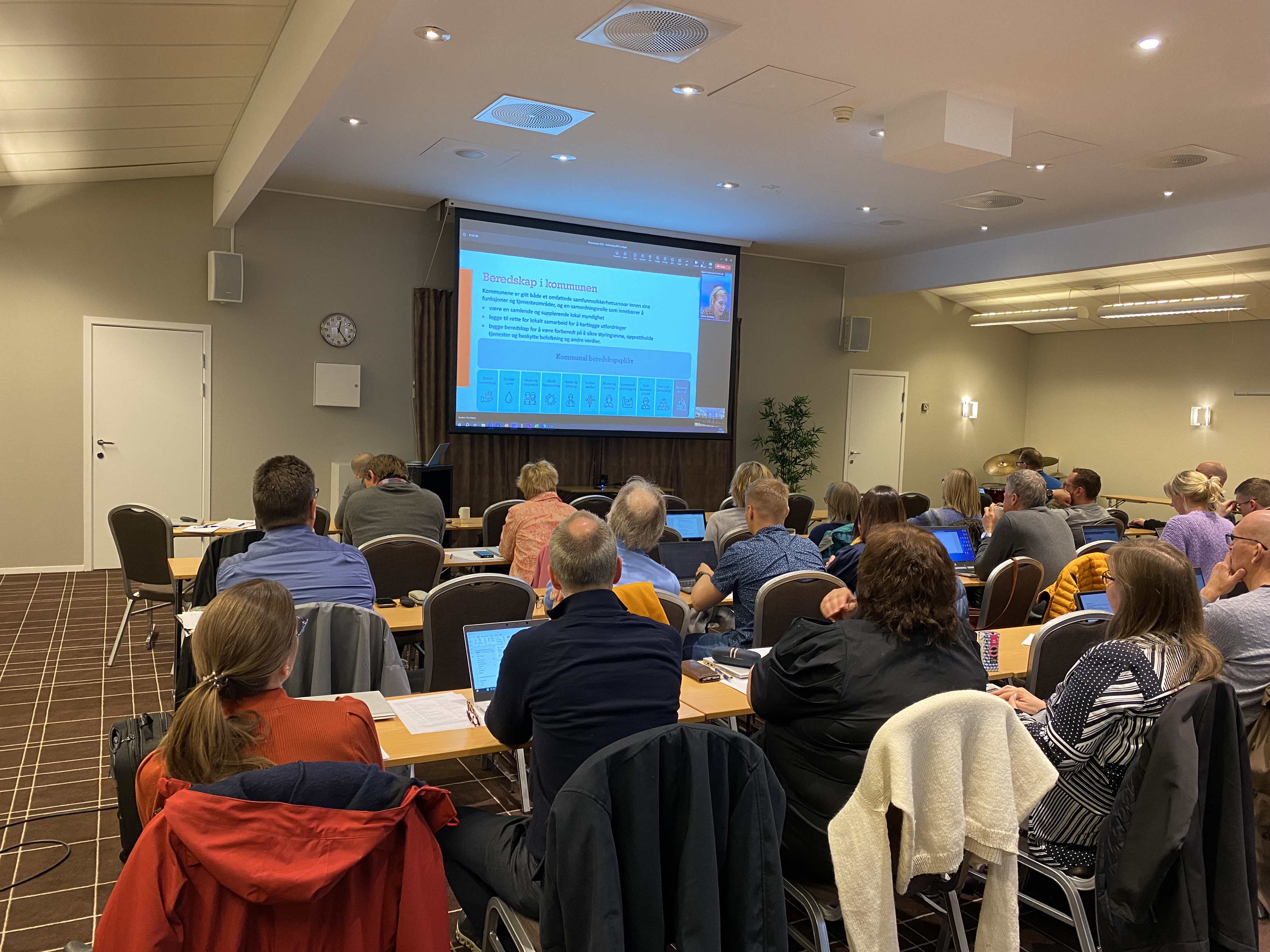 Deltakarane sit i møterommet, med ryggen til fotografen og ser mot ein powerpoint-presentasjon