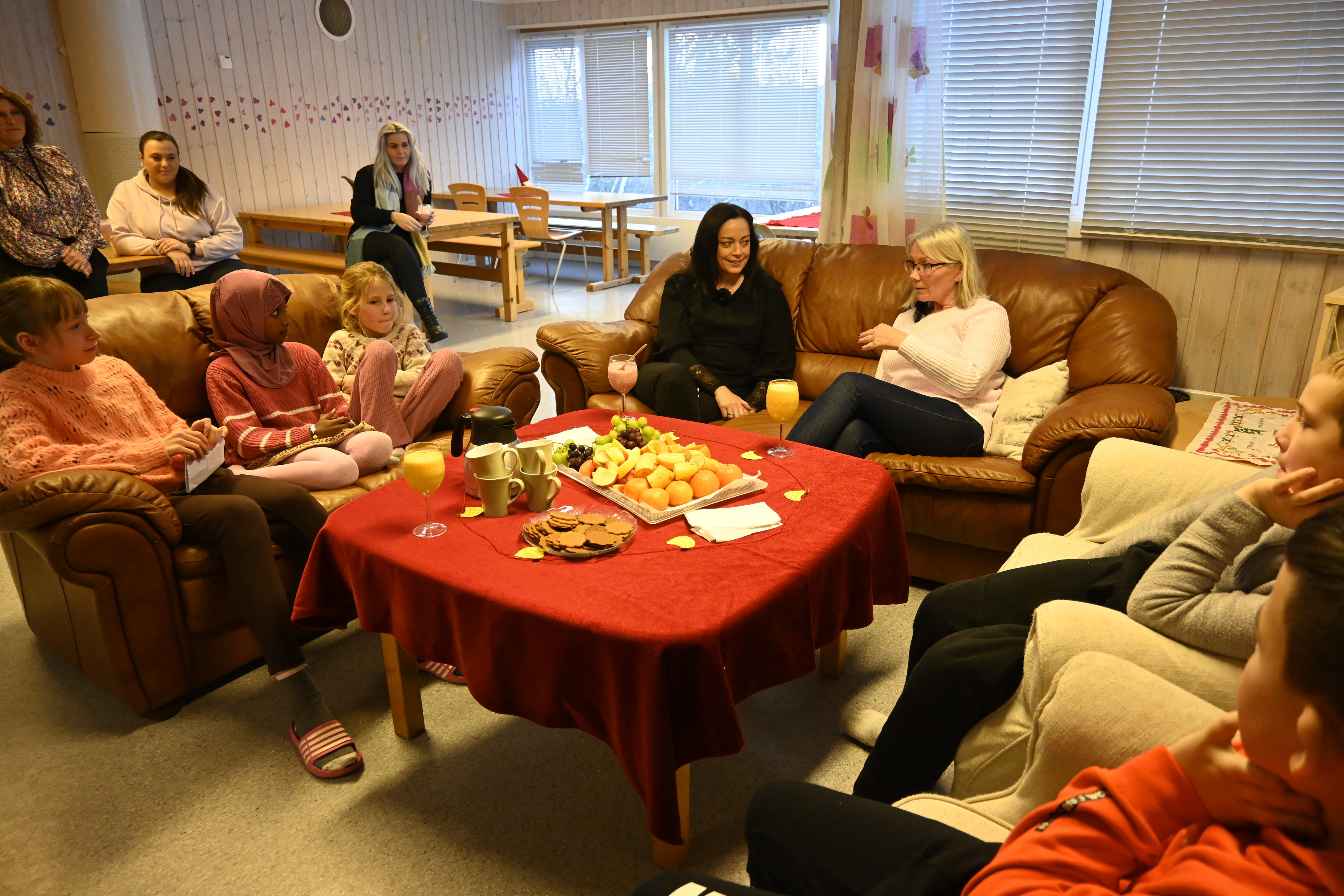Barn frå SFO sit  rundt fruktfatet i lag med statsforvaltar Else-May Norderhus og Berit Ulriksborg som leiar SFO. Foto: Elin Røshol