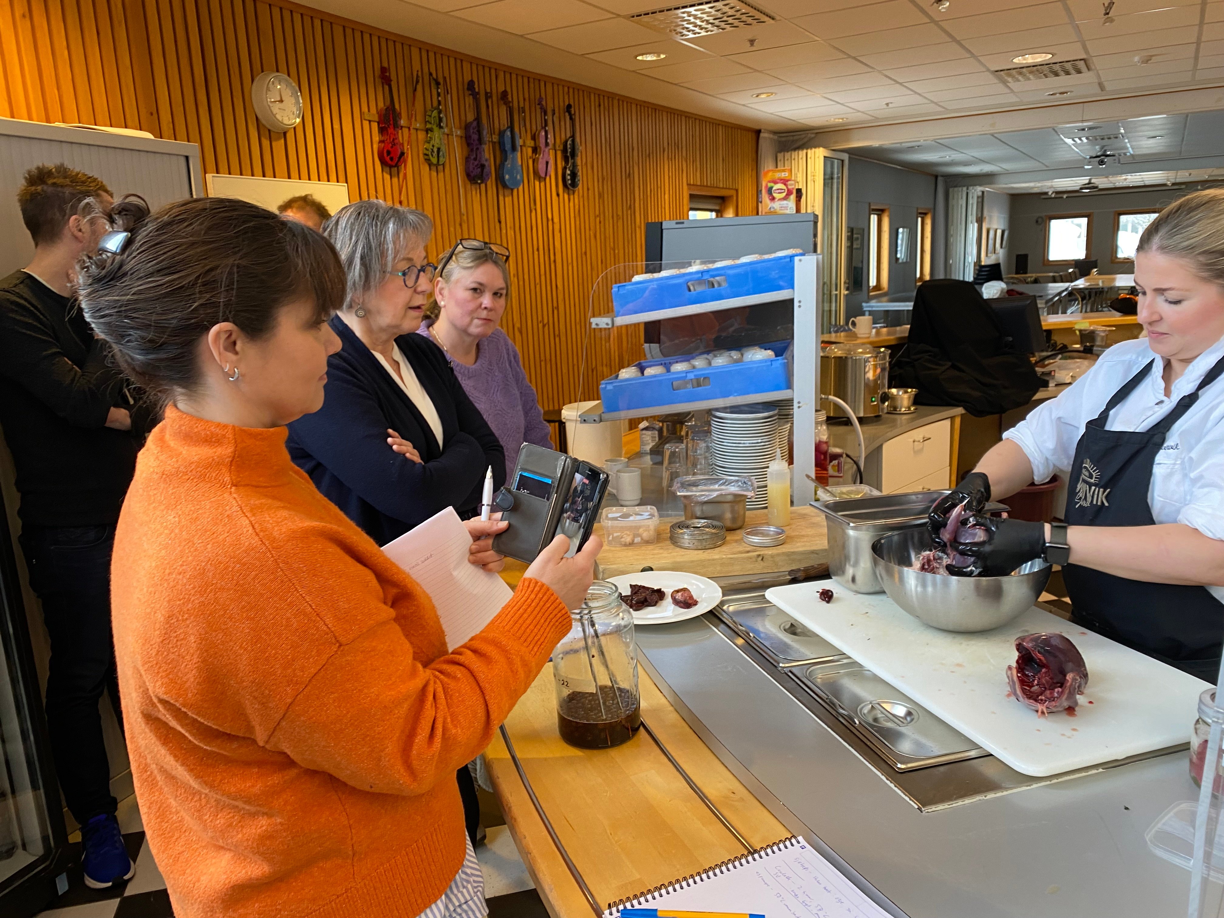 En dame står og skjærer i kjøtt. Flere står rundt og ser på. 