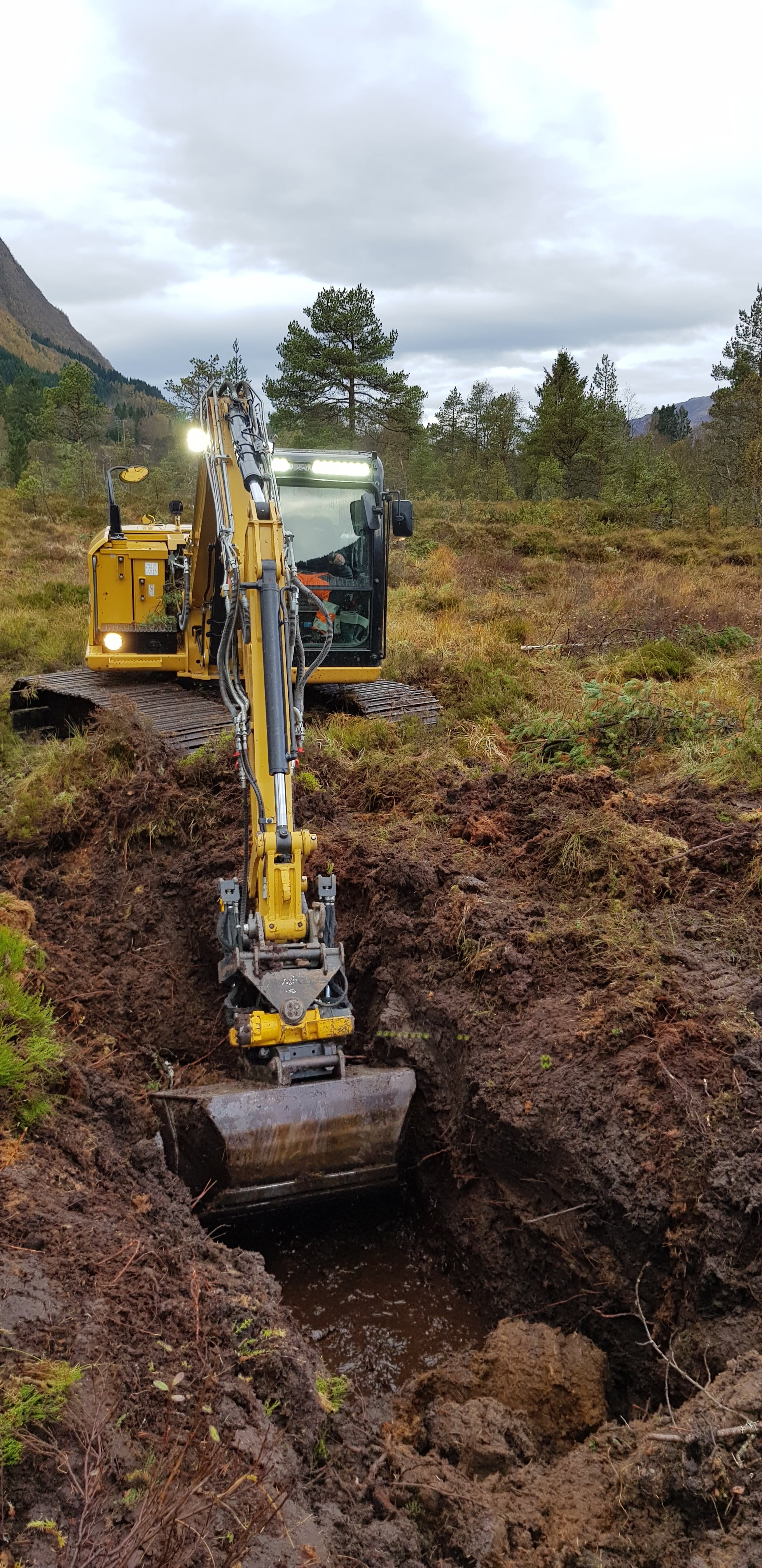 Avskjæring av lekkasje frå høgmyra. Gravemaskin lagar demning for å avskjære lekkasje av vatn frå høgmyra.