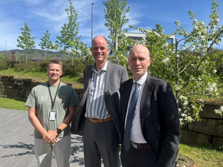 Tre menn står oppstilt med grønne trær bag seg.