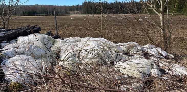 Fotografi av rundballeplast som er lagret ved siden av et jorde. 
