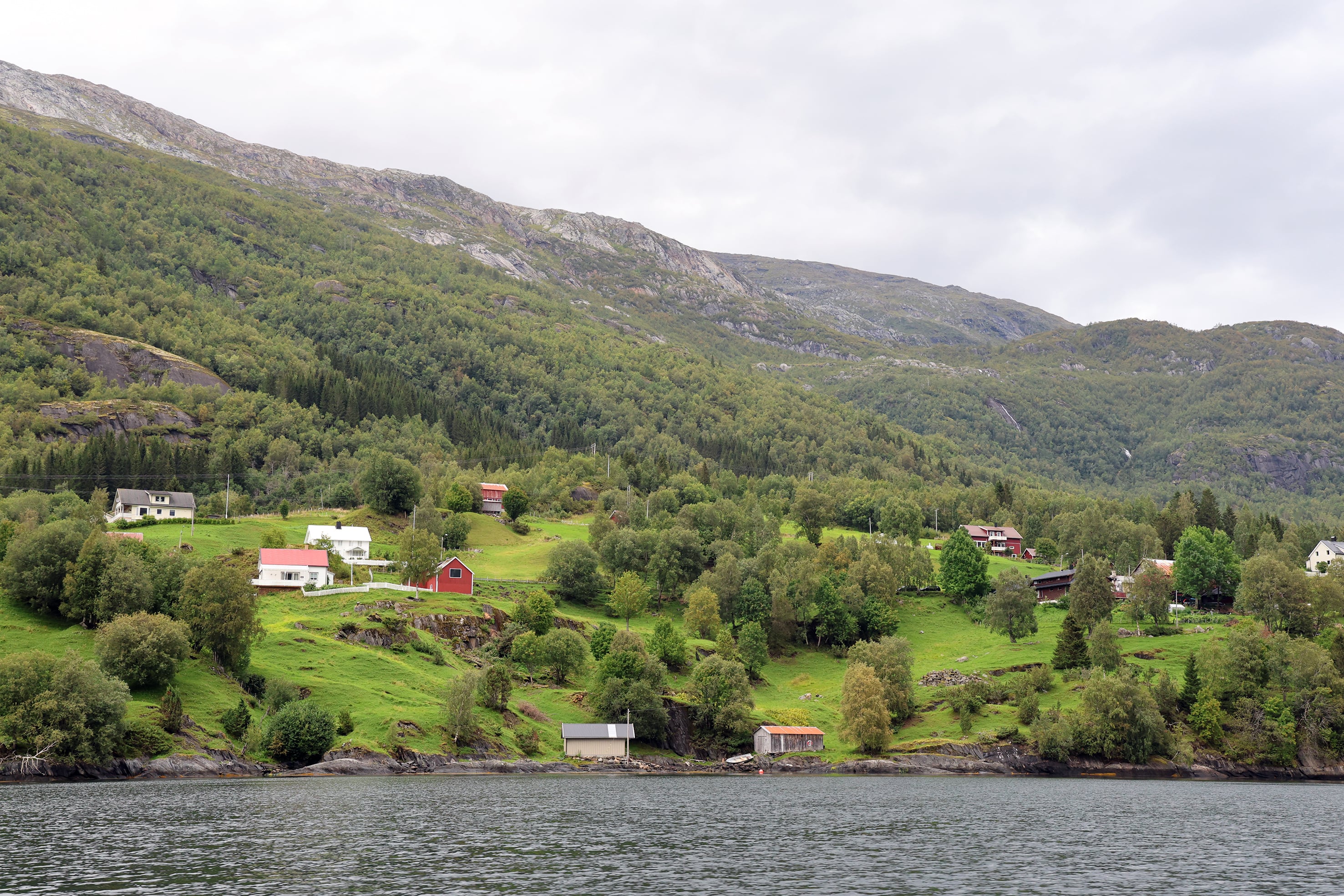 landskap med bygninger og grønne beitebakker ned mot en fjord 