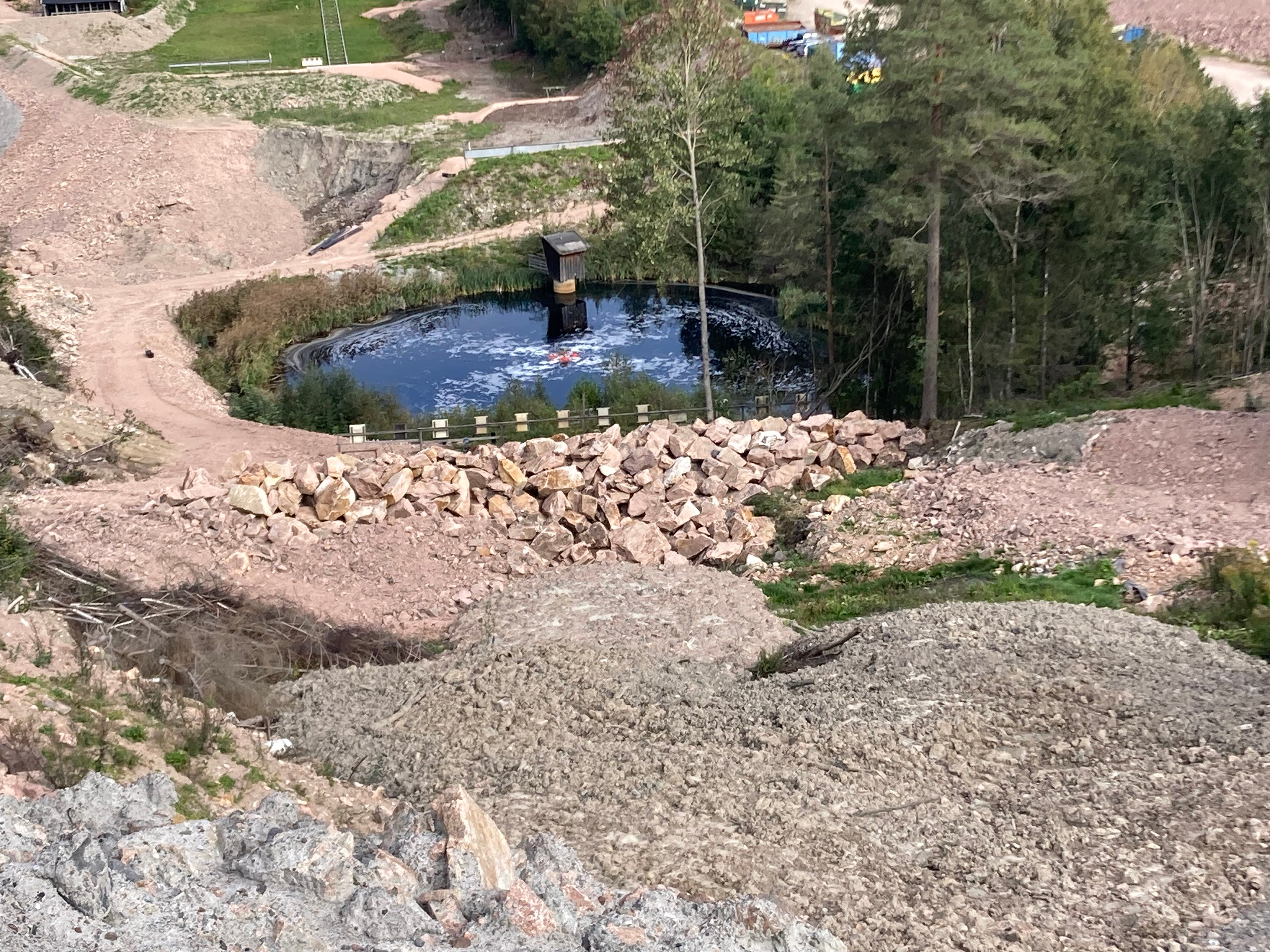 Bilde av en sigevannsdam på et avfallsdeponi. Ligger jord- og steinmasser på anleggsområdet, men og et lite grøntområdet rundt selve sigevannsdammen.