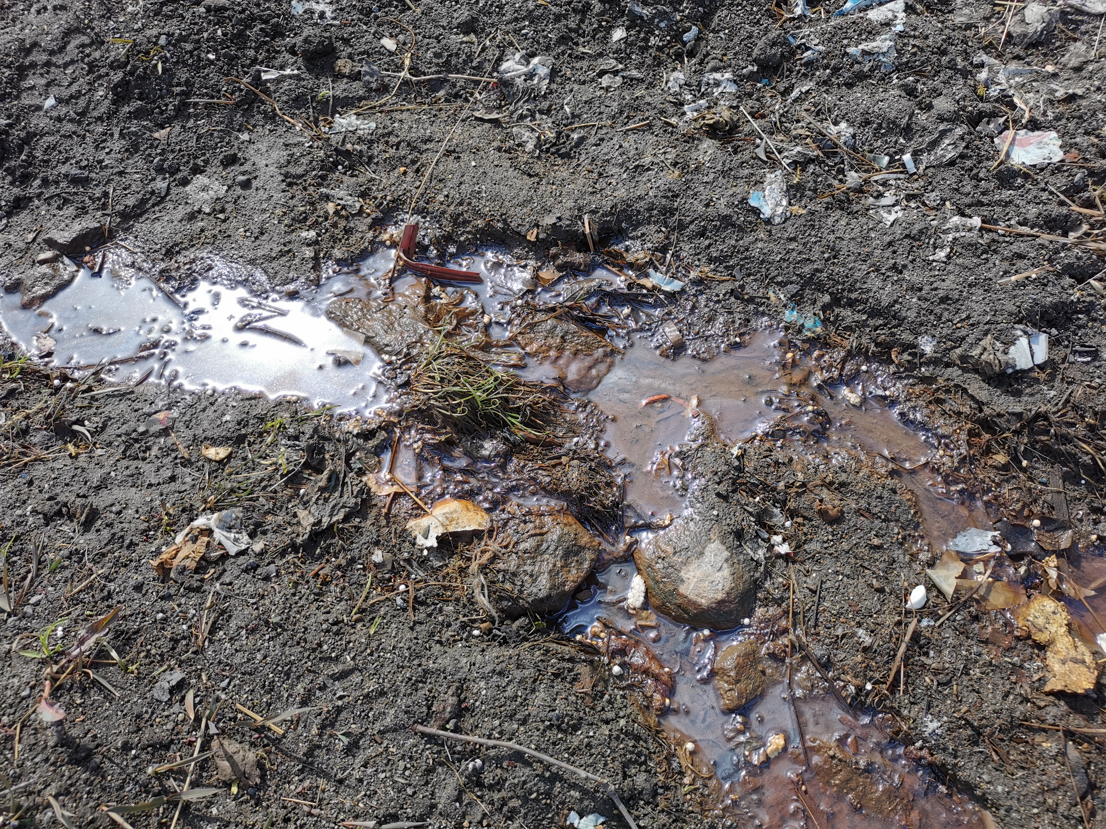 Forurenset jord- og steingrunn med brunt og forurenset vann med fragmenter av avfall og plast