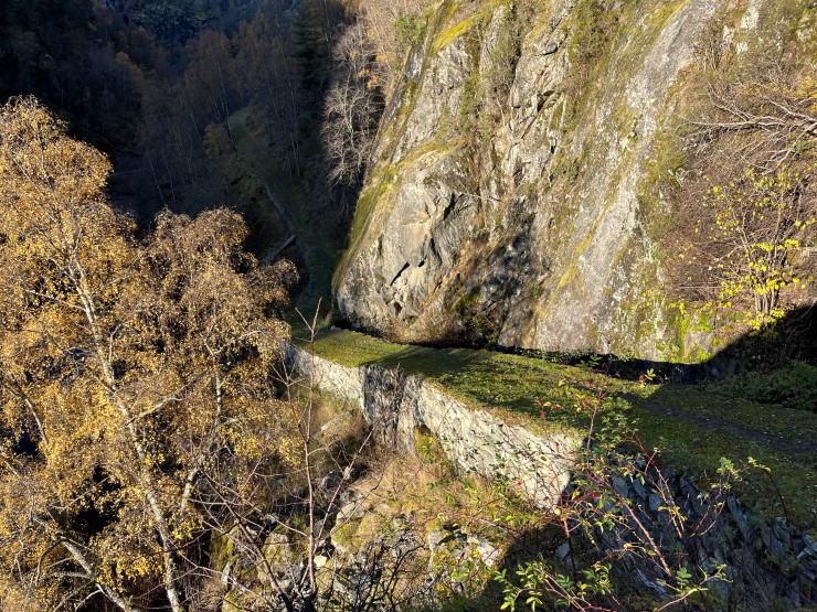 ein steinmur langs ein veg med fjellskrent over og låg sol