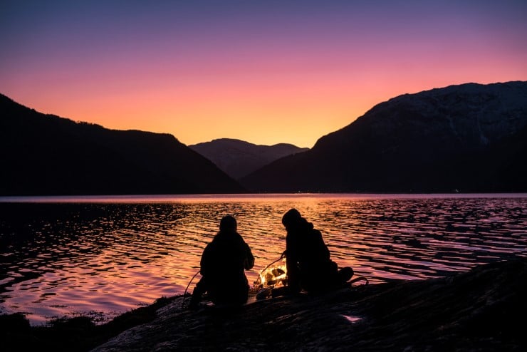 to personar brenn bål med fjorden og vakker himmel i bakgrunnen