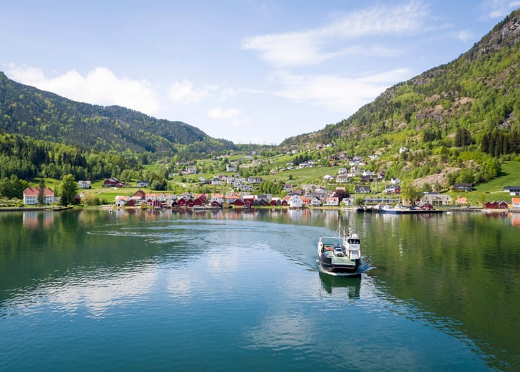 ei ferje kjem mot deg frå ein liten tettstad langs fjorden med blå himmel