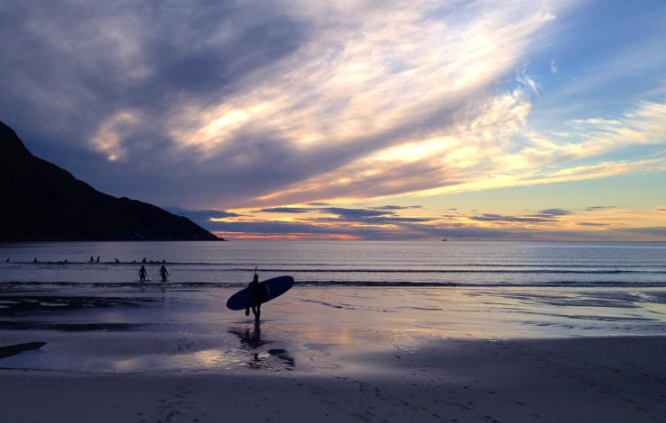 surfere på ei strand med roleg vatn og fargerik himmel 