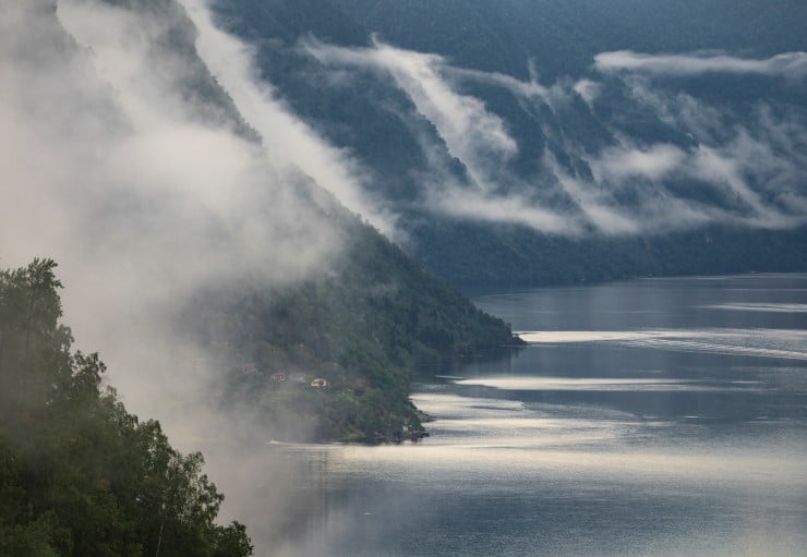 Lågt skydekke langs fjorden med ein bustad på eit nes