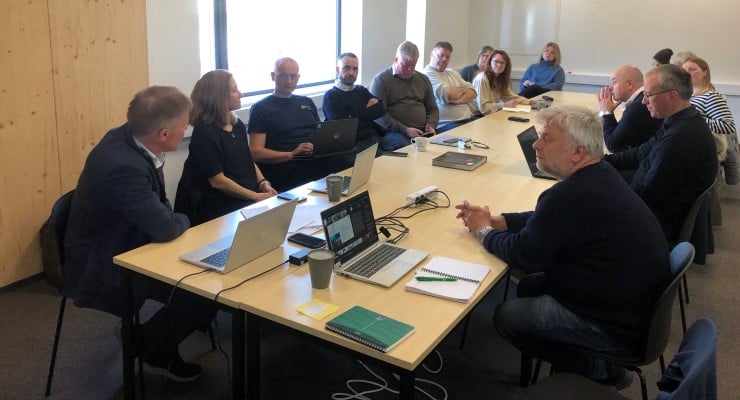 Mange menneskje rundt eit møtebord, god stemning. 