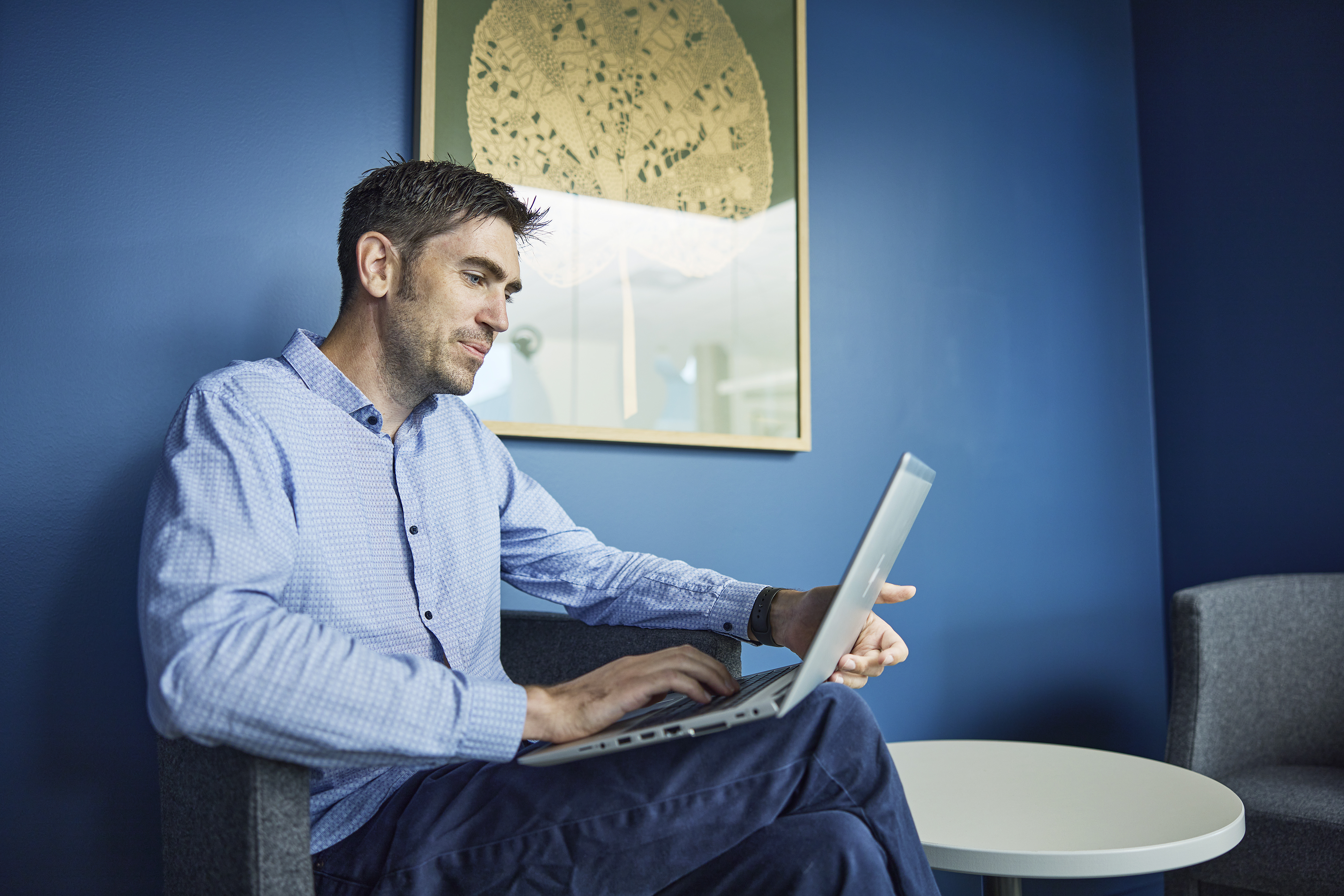 Mann sitter og jobber avslappet p&aring; en laptop