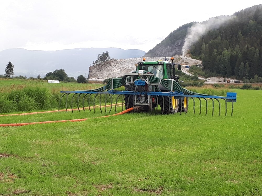Traktor med tilførselslange for spredning av husdyrgjødsel på et grønt jorde.