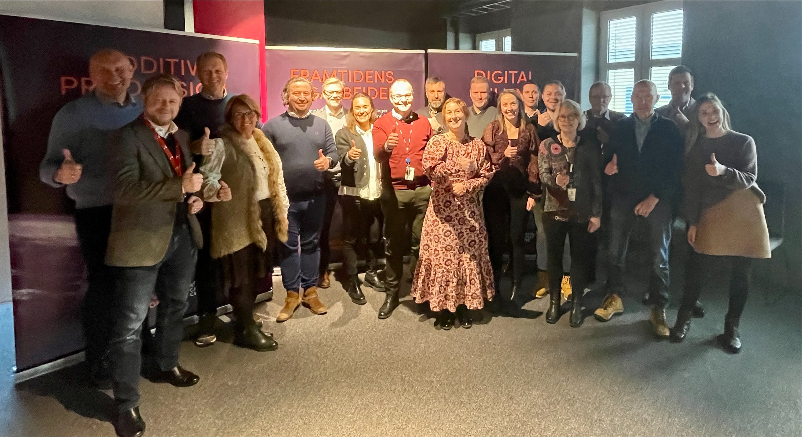 Omtrent 20 personer oppstilt i et lokale foran bannere om innovasjon i industrien