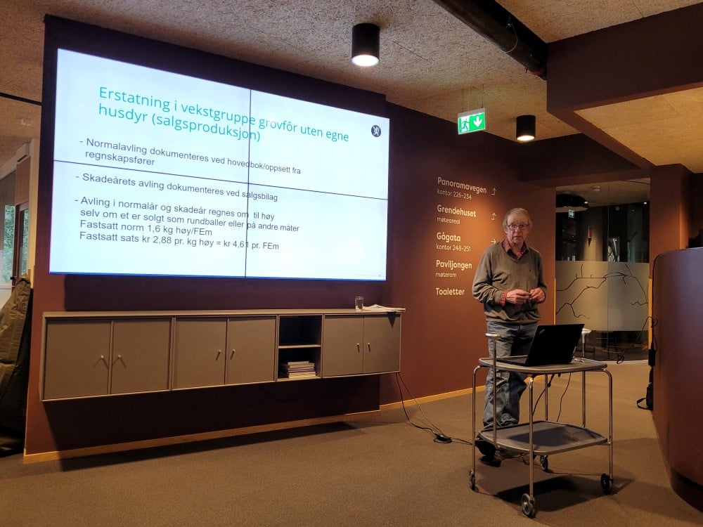 Mann som held innlegg og brukar PC til presentasjon på skjerm på veggen