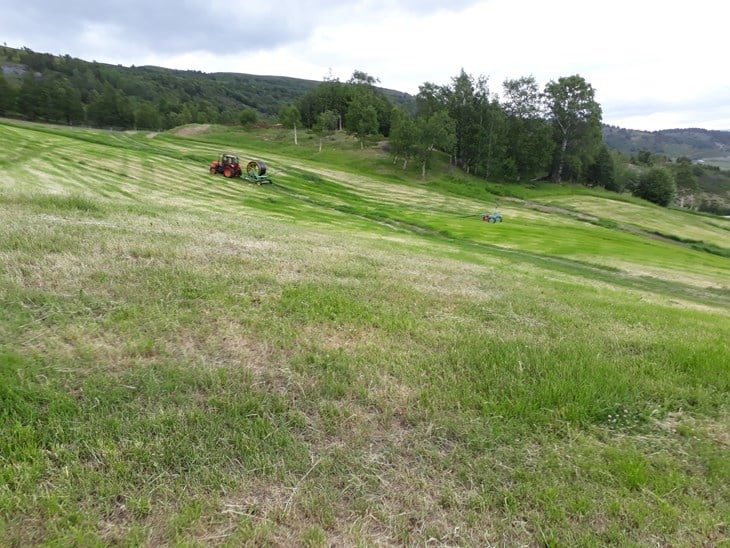 Et jorde med delvis tørkeskadet grasmark. En traktor drar vanningsmaskin.